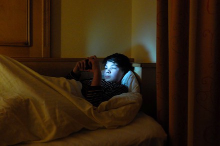 Ein Jugendlicher  in seinem Bett mit Smartphone